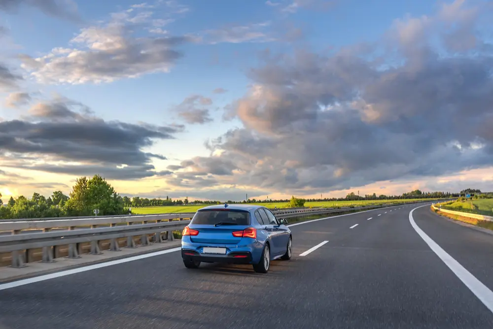Blauwe auto rijdt op een lege snelweg bij zonsondergang.