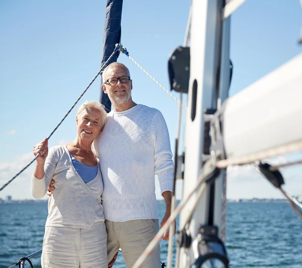 Een ouder echtpaar poseert samen op een zeilboot met een blauwe lucht en zee op de achtergrond.