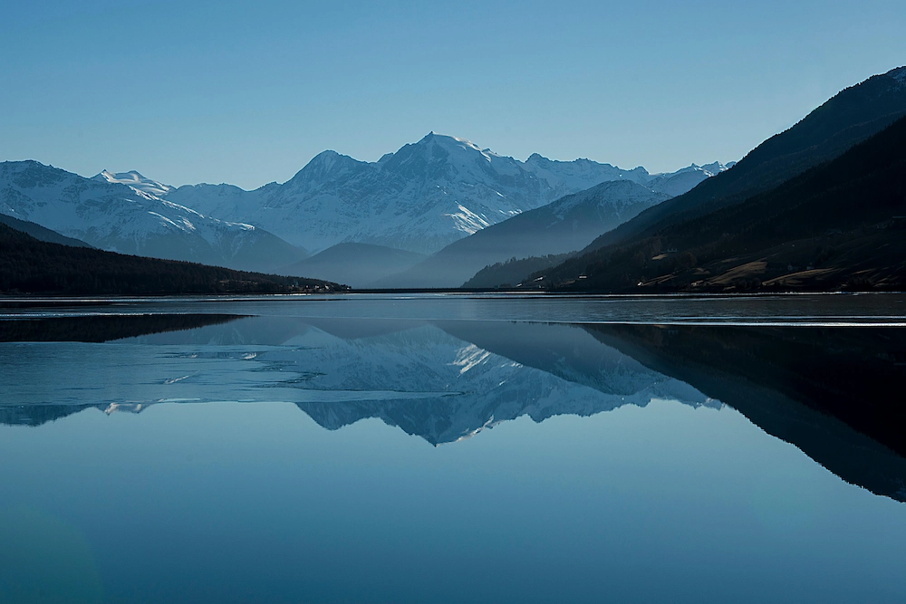 Een serene berglandschap met besneeuwde toppen weerspiegeld in een kalm meer.