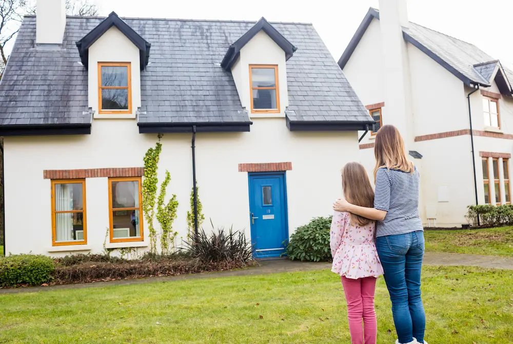 Een vrouw en een kind staan voor een huis met een blauwe voordeur.