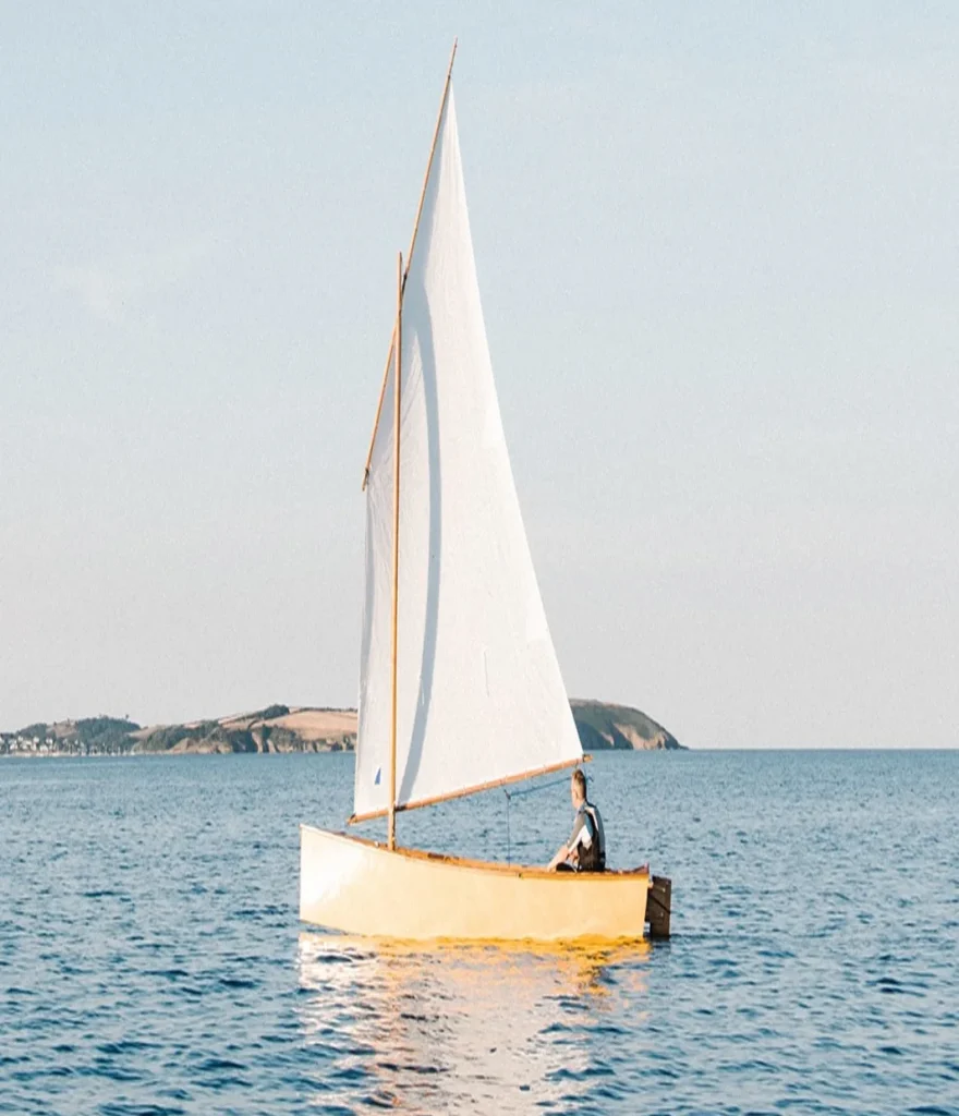 Een persoon zeilt alleen in een kleine boot op een rustige zee met een heldere lucht.