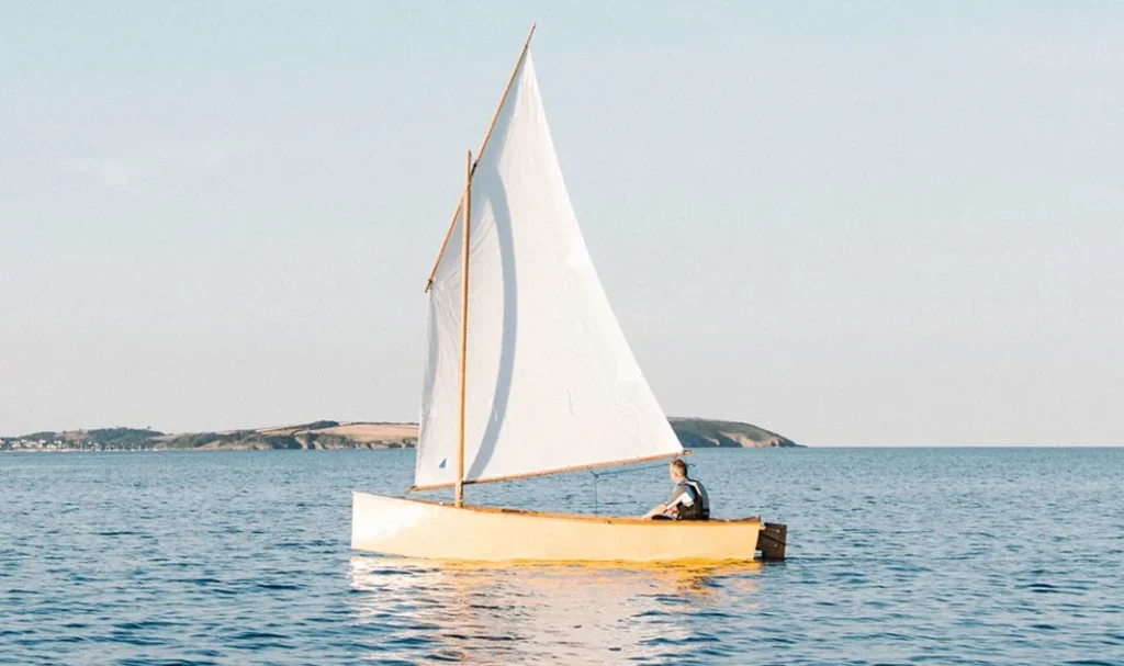 Een zeilboot met witte zeilen vaart op een rustige zee met een kustlijn op de achtergrond.